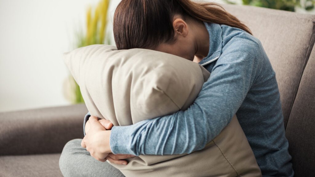 kvinde, der sidder i sofa med hovedet i og armene om en pude som billede på nedsmeltning hos voksne med autisme